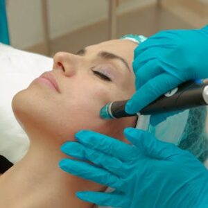A woman receiving a facial skincare treatment with a specialized device wearing protective gloves.