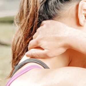 A woman massages her neck outdoors, relieving discomfort and tension.