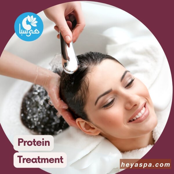 A woman smiling with her eyes closed as her hair is being washed after did hair protein and keratin treatment in a salon, with a hairdresser's hand holding a shower head to pour water over her hair.